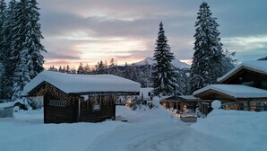 Un refugio cubierto de nieve con fachada de madera, rodeado de árboles cargados de nieve y una montaña al fondo.