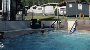 Una piscina con una persona en el agua, rodeada de casas y montañas al fondo.