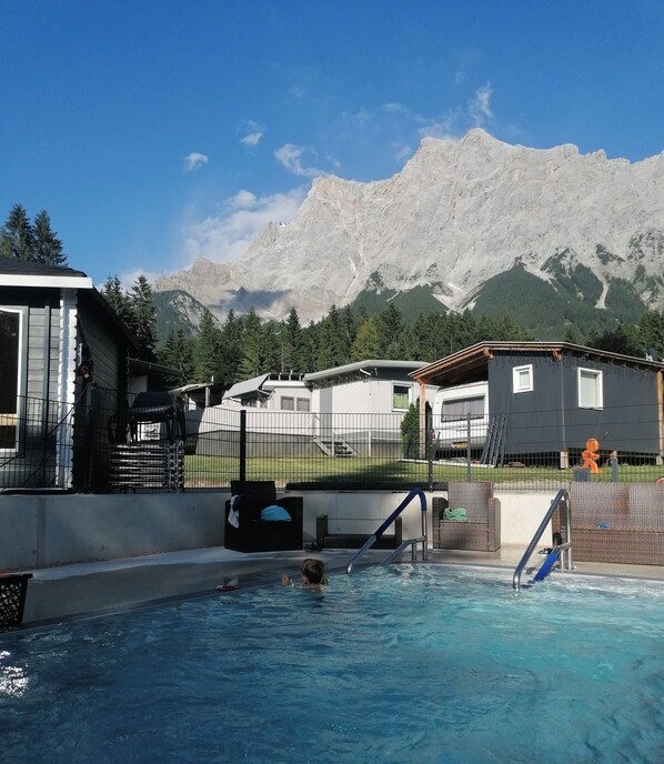 A swimming pool with a person in the water, surrounded by houses and mountains in the background.