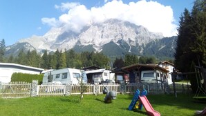 Un camping con vehículos recreativos, un parque infantil y montañas al fondo.