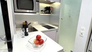 Una cuina moderna amb microones, cafetera i un bol de fruita al taulell.
