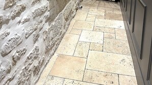 Un mur de pedra amb un armari metàl·lic, un terra de rajoles i una porta negra.