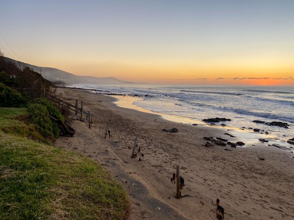A beach with a wooden fence, a grassy area, and a rocky shoreline.