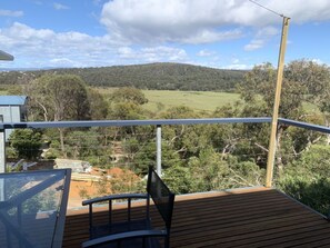 A deck with a view of a rural landscape, including fields and hills.