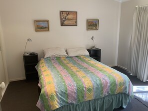 A bedroom with a bed, two bedside tables, a lamp on each table, and three framed pictures on the wall.