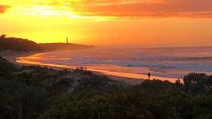 Un coucher de soleil sur une plage, avec un phare visible au loin.