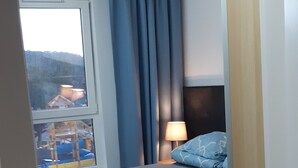 Une chambre à coucher avec un lit, une table de chevet, une lampe et une fenêtre avec des rideaux.