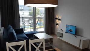 Un salon moderne avec un canapé, une table à manger, un téléviseur et une vue sur une piscine et des bâtiments à l’extérieur.
