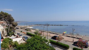 Un passeig marítim amb vista despejada al mar, un camí pavimentat i cotxes aparcats.