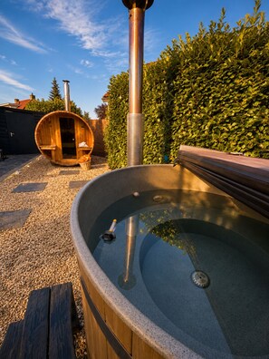 Una vasca idromassaggio con un molo di legno, una sauna in legno e un camino in metallo.
