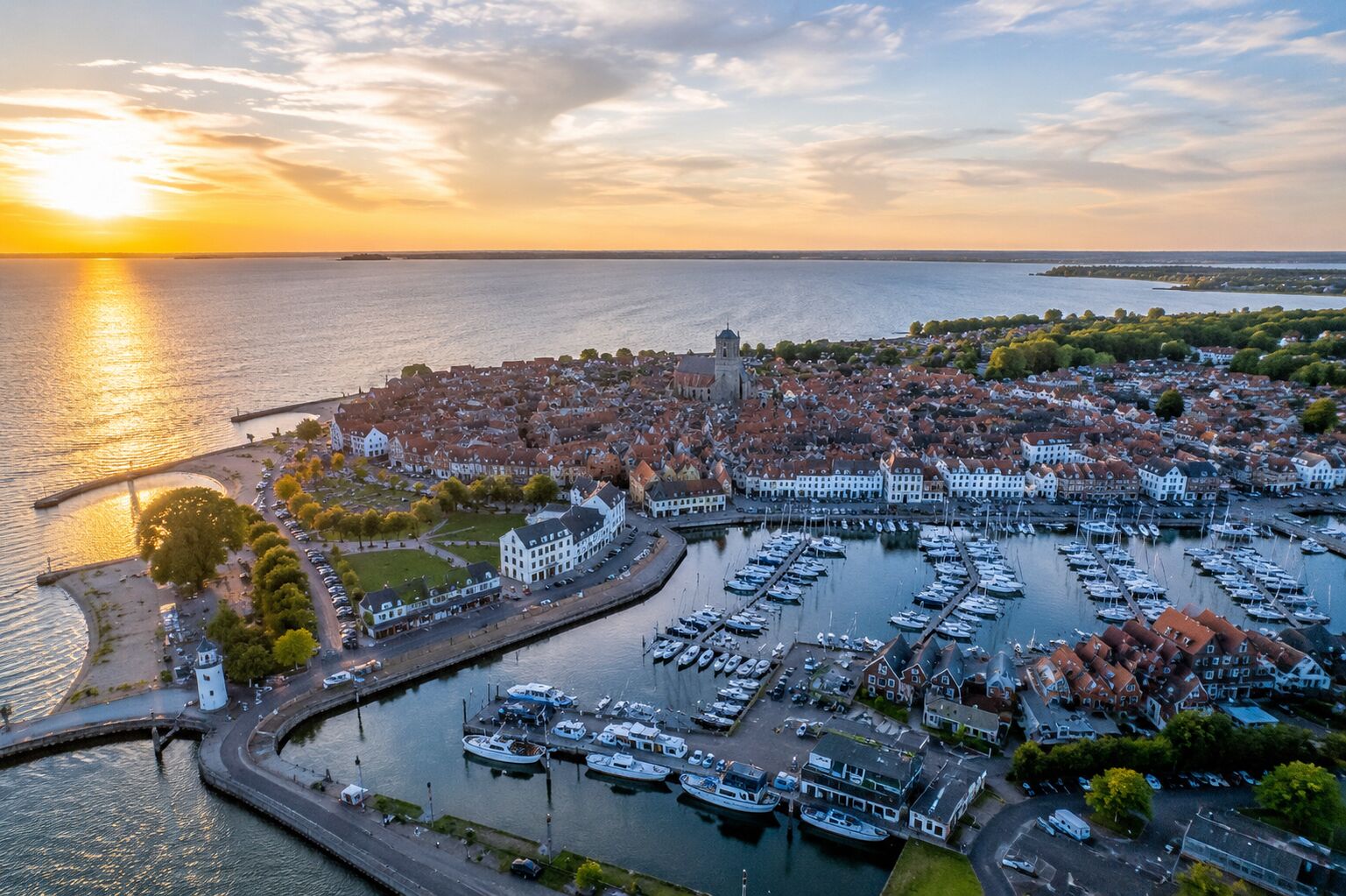 Vue aérienne d’une ville côtière avec un port de plaisance, des bâtiments donnant sur le front de mer et un clocher d’église imposant.
