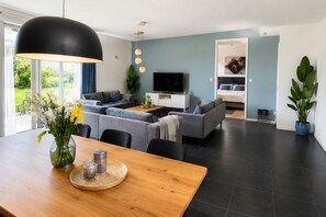 Un salon moderne avec un ensemble de canapés, une table à manger agrémentée d’un vase de fleurs et un téléviseur.