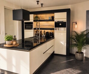 Une cuisine moderne dotée d’un îlot central, d’appareils électroménagers intégrés et d’une plante en pot.