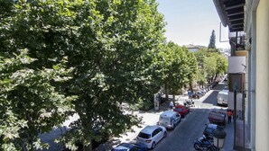 Une vue de rue avec des voitures garées, des arbres et un immeuble doté d’un balcon.