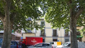 Une scène de rue avec des voitures garées, un camion de livraison rouge et un immeuble doté de balcons.