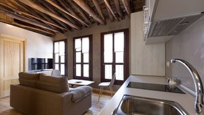 Eine moderne Küche mit integriertem Spülbecken, ein Essbereich mit Tisch und Stühlen sowie ein Sofa in einem Wohnzimmer mit großen Fenstern.