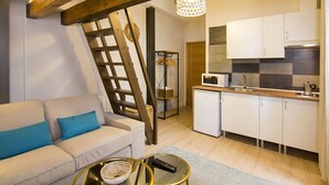 Un espacio habitable pequeño con un sofá, una escalera, una cocina con armarios blancos y una lámpara colgante.