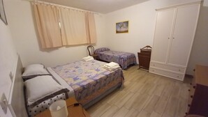 A bedroom with two beds, a wardrobe, a chair, and a small table.
