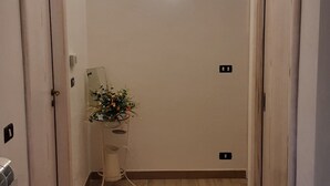 A hallway with wooden flooring, a small table with a vase of flowers, and two doors.
