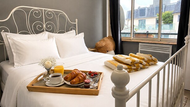 A neatly made bed with white linens, a tray with croissants, a cup of coffee, and a glass of orange juice. - L'appartement des Champs Elysées (Paris)