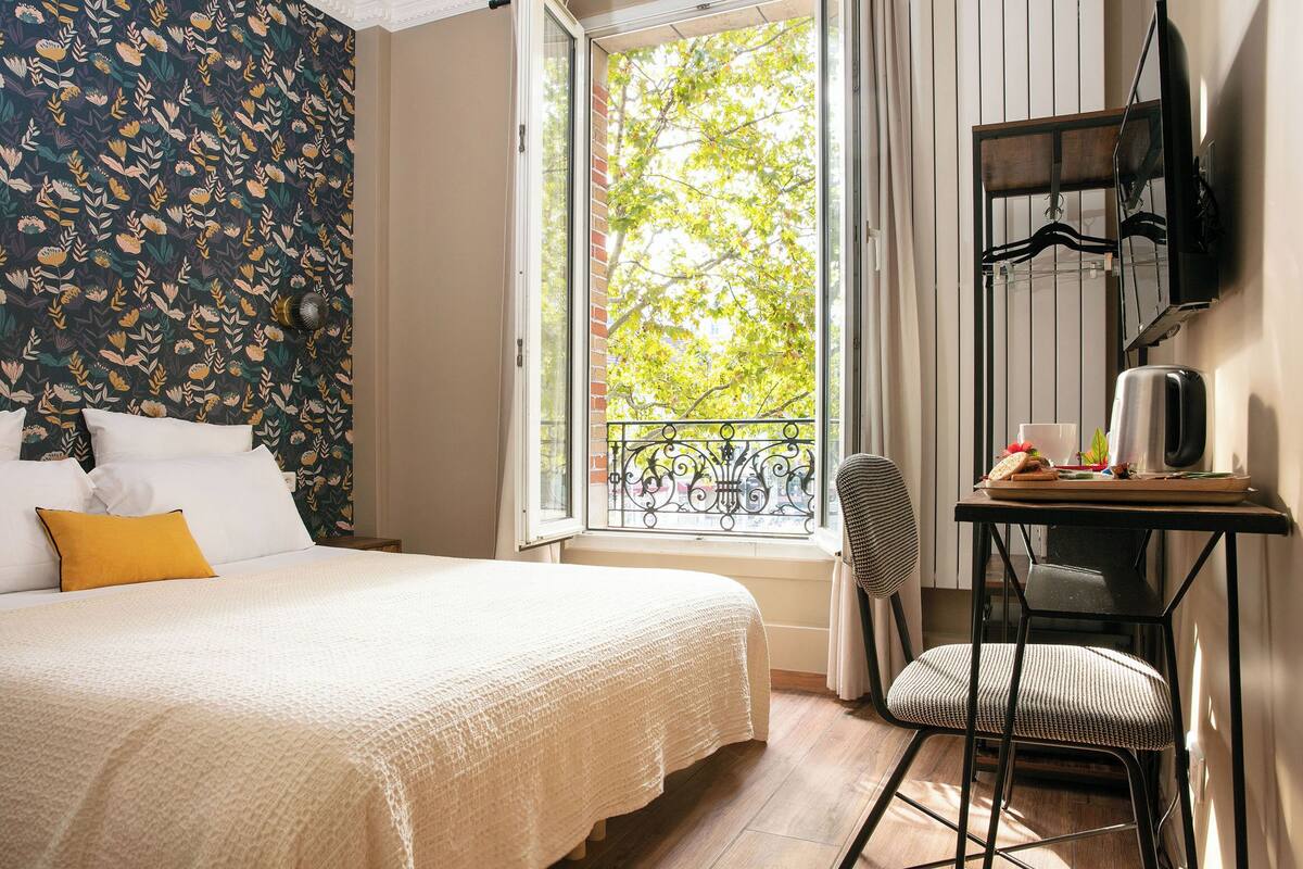 A bedroom with a bed, a chair, a table, and a window with a view of trees.