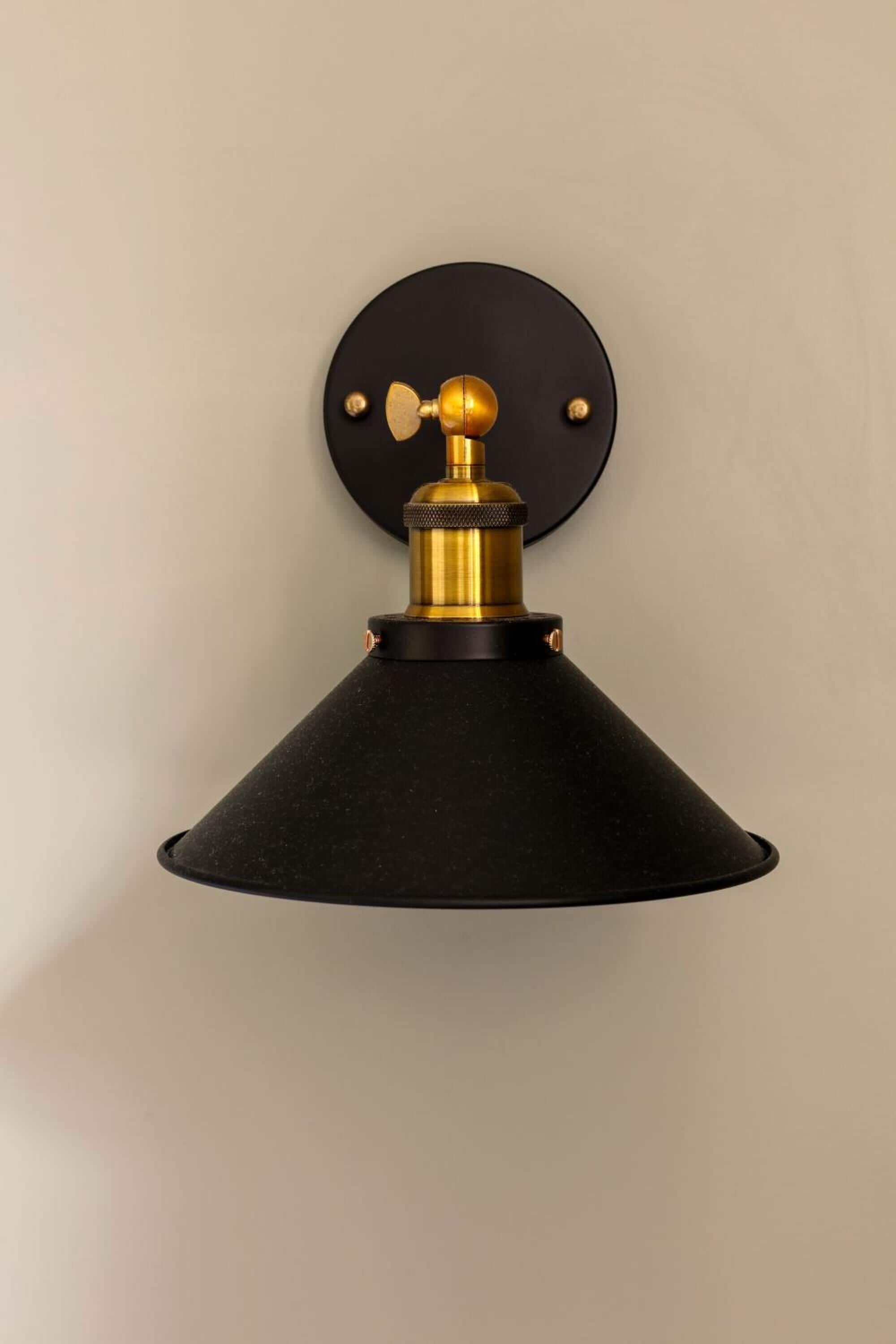 A wall-mounted lamp with a black shade and brass accents.