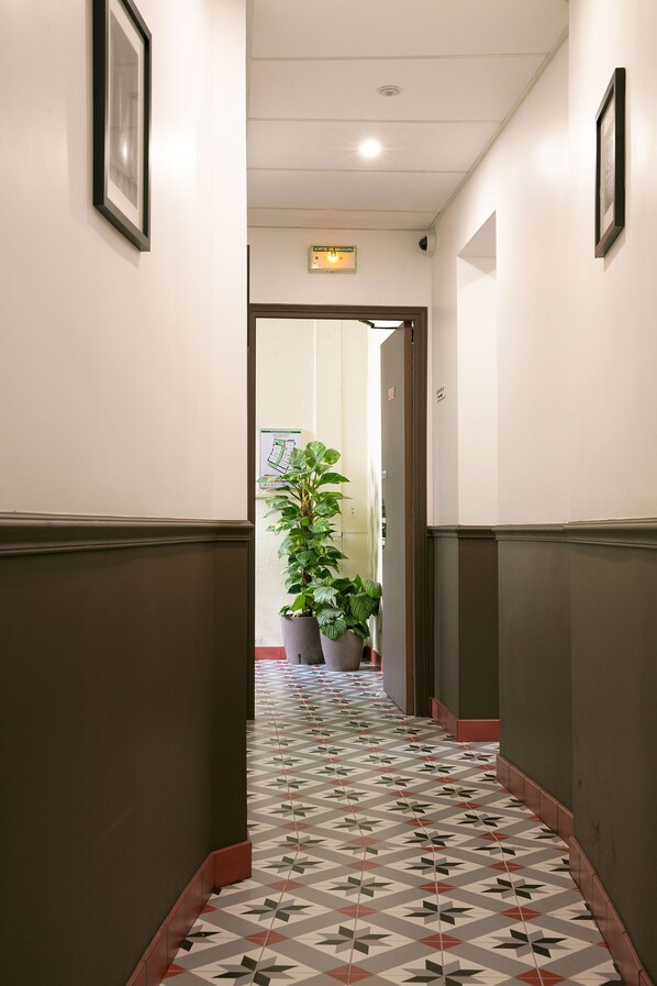 A hallway with patterned flooring, potted plants, and framed pictures on the walls. - Le Grand Albert 1er (Maisons-Alfort)