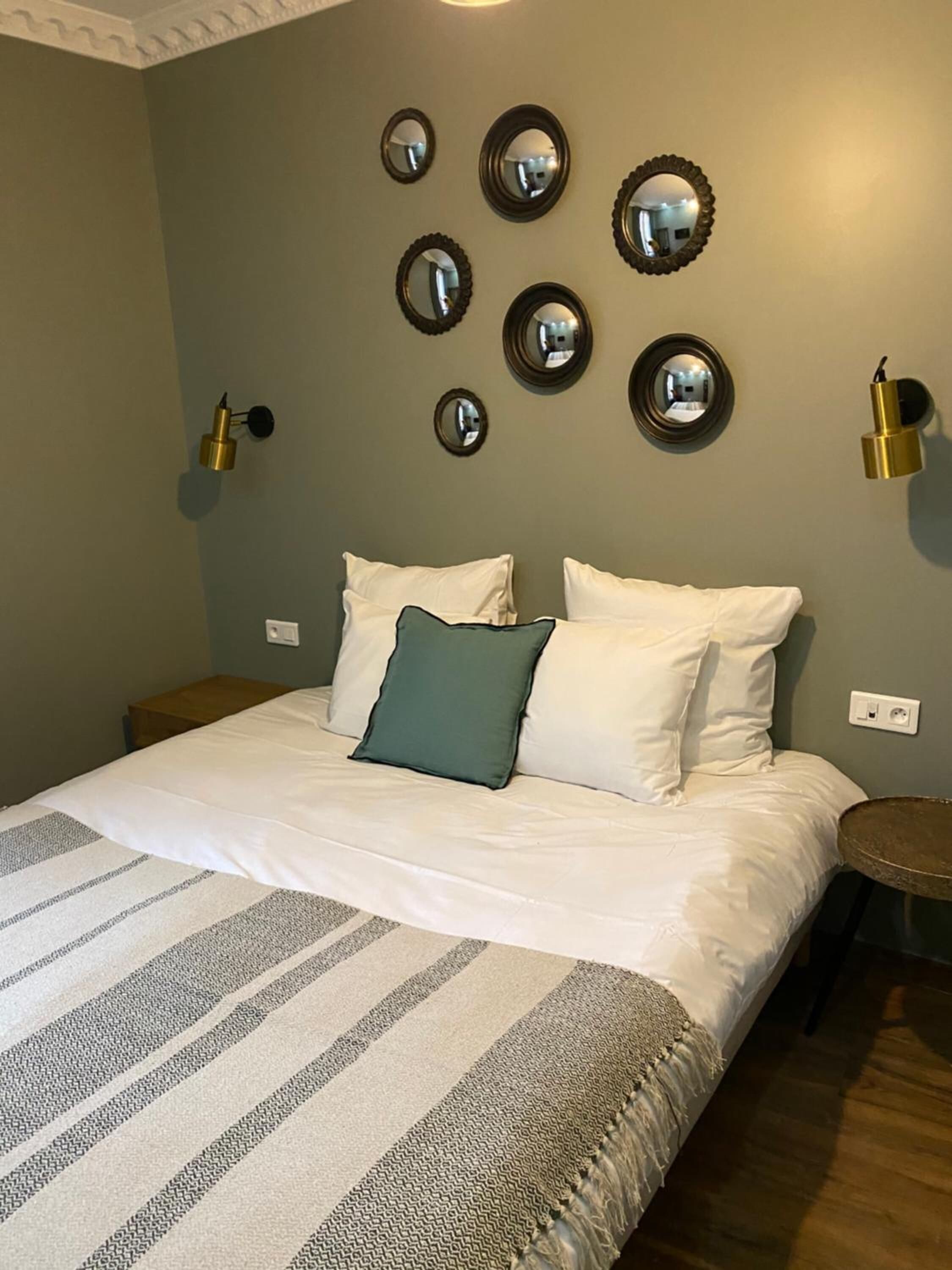 A neatly made bed with white and gray striped bedding, a green pillow, and a small round table beside it.