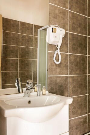 A bathroom with a white sink, a hairdryer mounted on the wall, and a mirror above the sink. - Le Grand Albert 1er (Maisons-Alfort)