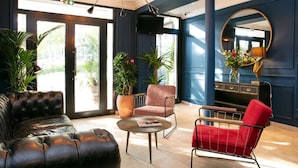 Un vestíbulo moderno con sofás de cuero, una mesa redonda para café y un sillón rojo. Hay plantas grandes en macetas y un espejo en la pared.