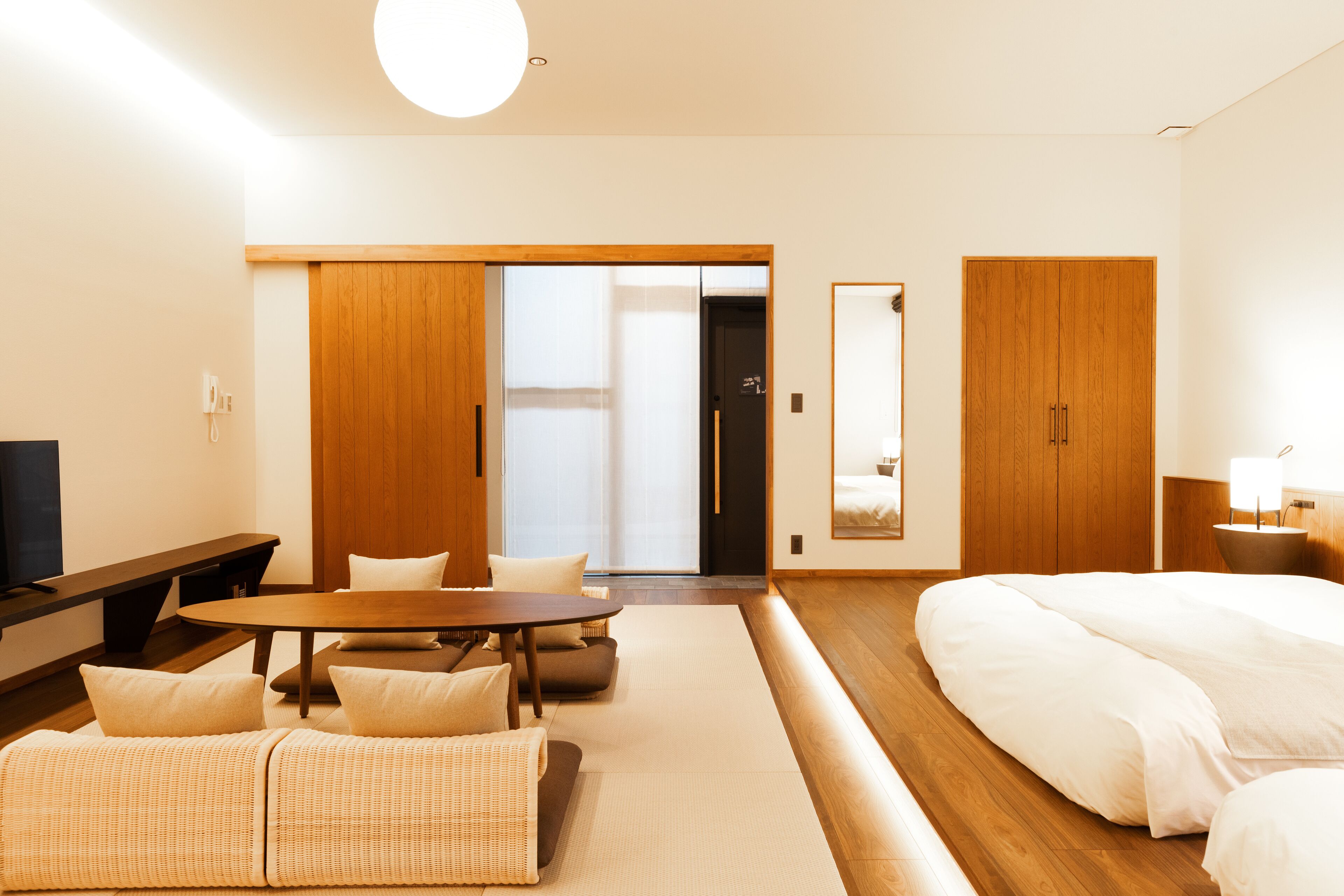 Una habitación de hotel moderna con suelo de madera, un sofá, una mesa de comedor, una cama y un espejo grande.