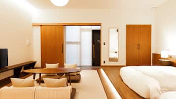 Una habitación de hotel moderna con suelo de madera, un sofá, una mesa de comedor, una cama y un espejo grande.