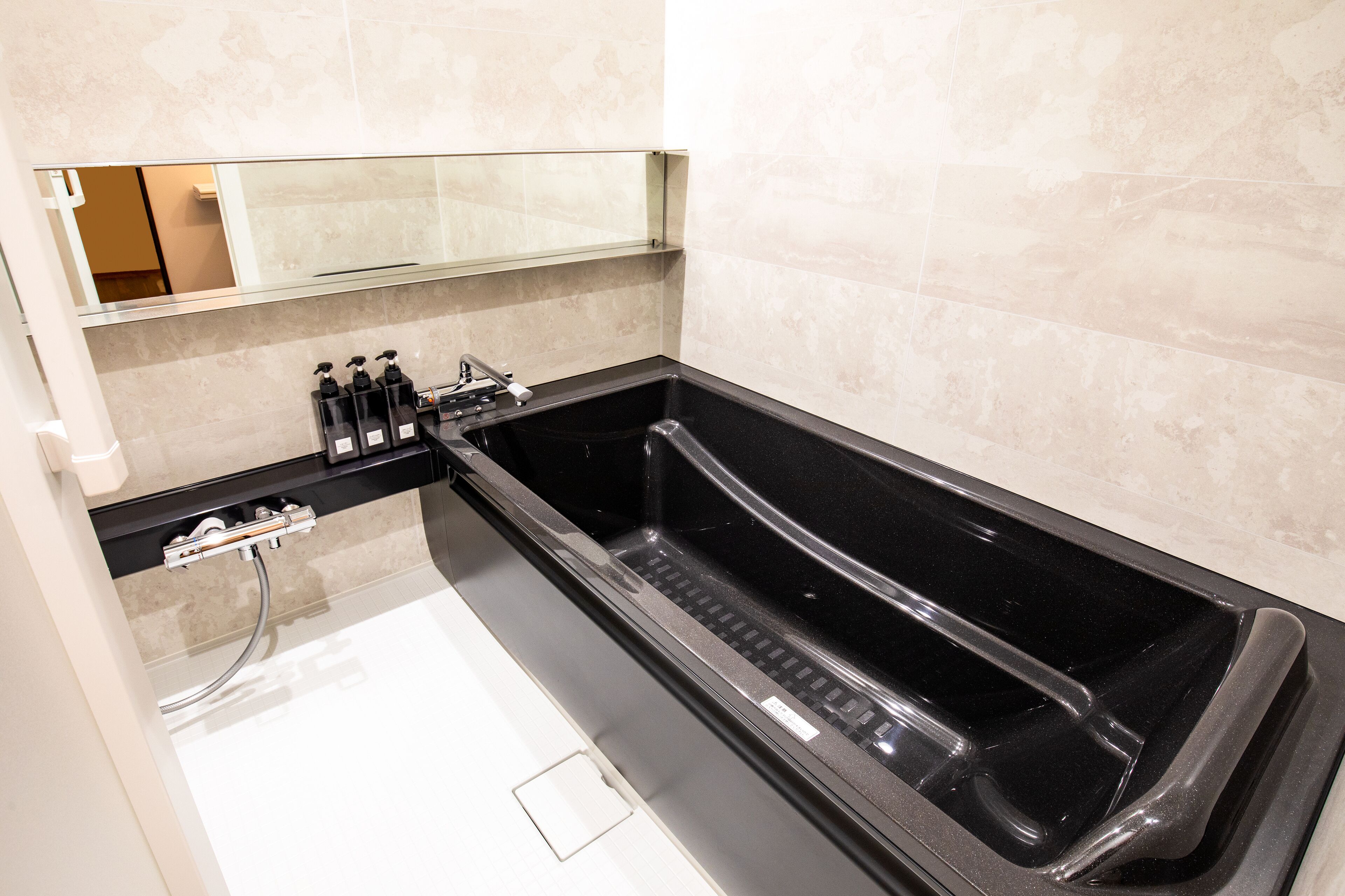 A modern bathroom with a black bathtub, a glass shower enclosure, and a mirror above the sink.