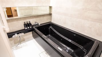 A modern bathroom with a black bathtub, a glass shower enclosure, and a mirror above the sink.