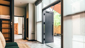 A modern interior with a wooden floor, a green sofa, a sliding glass door leading outside, and a visible outdoor area with a wooden fence. - Hotel Karuizawa Cross (Karuizawa)