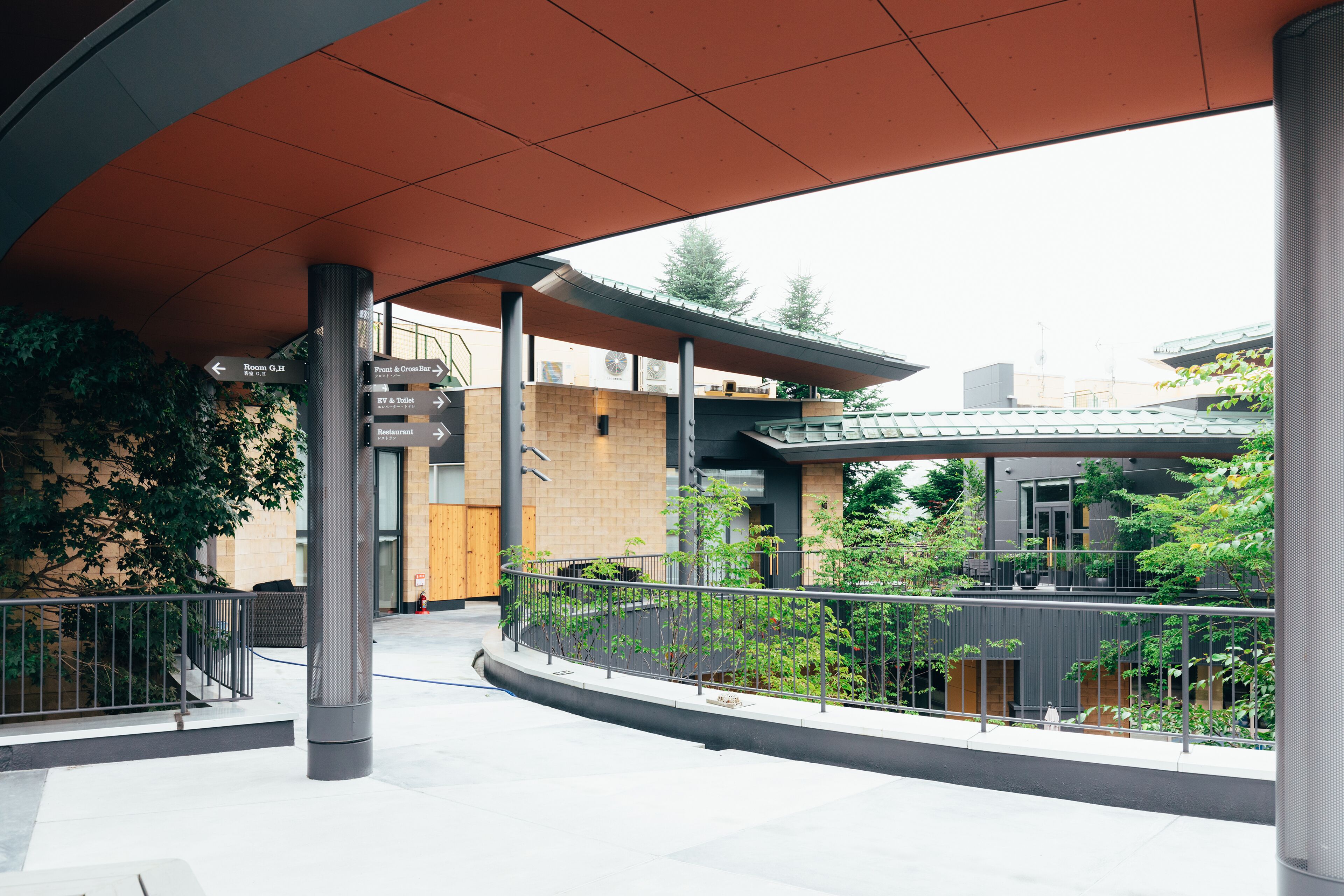 Un espacio al aire libre con un paseo techado, señalización direccional y vistas a edificios y vegetación.