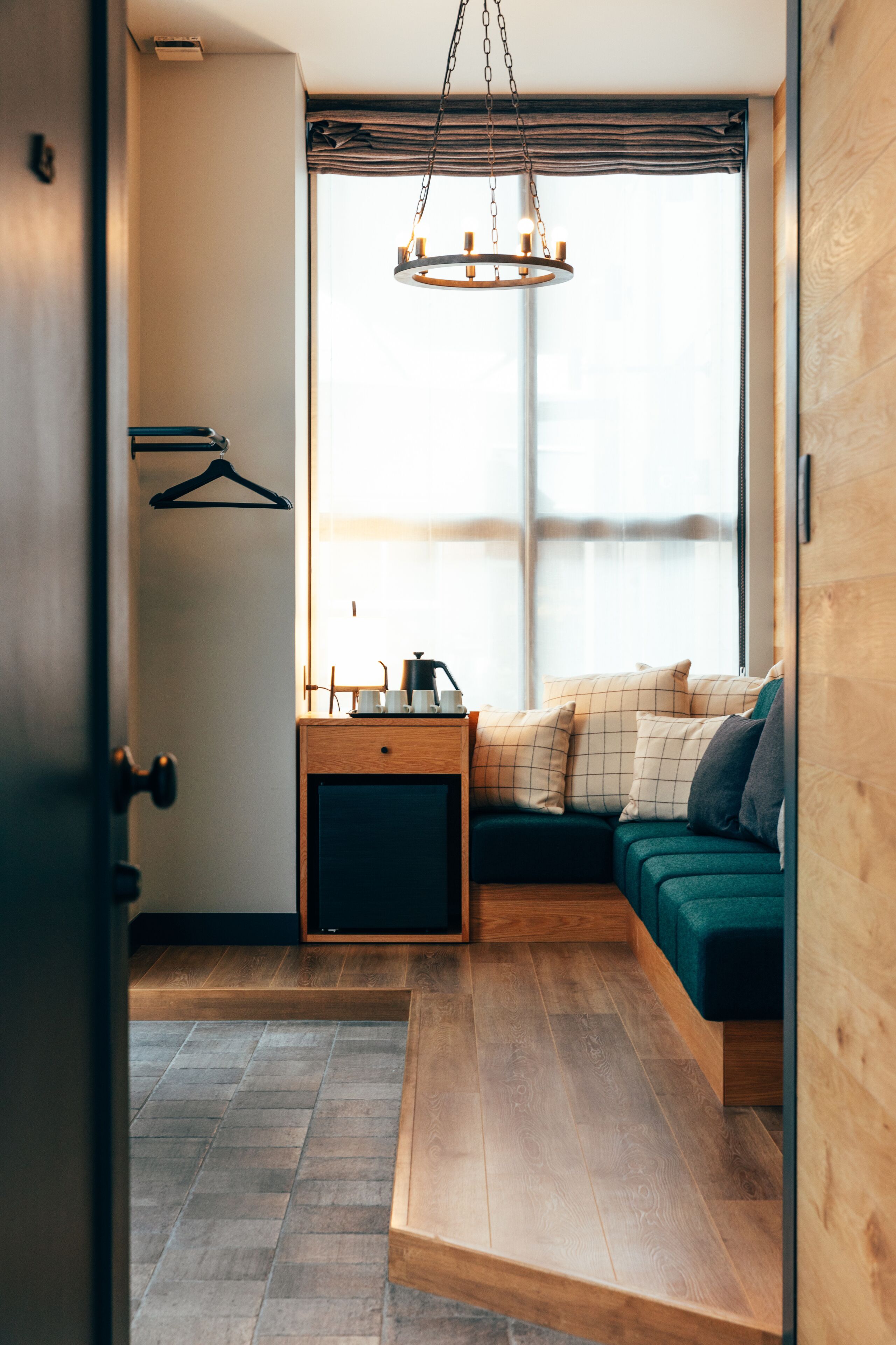 A cozy room with a wooden floor, a green sofa with cushions, a small wooden table with a kettle, and a hanging light fixture.