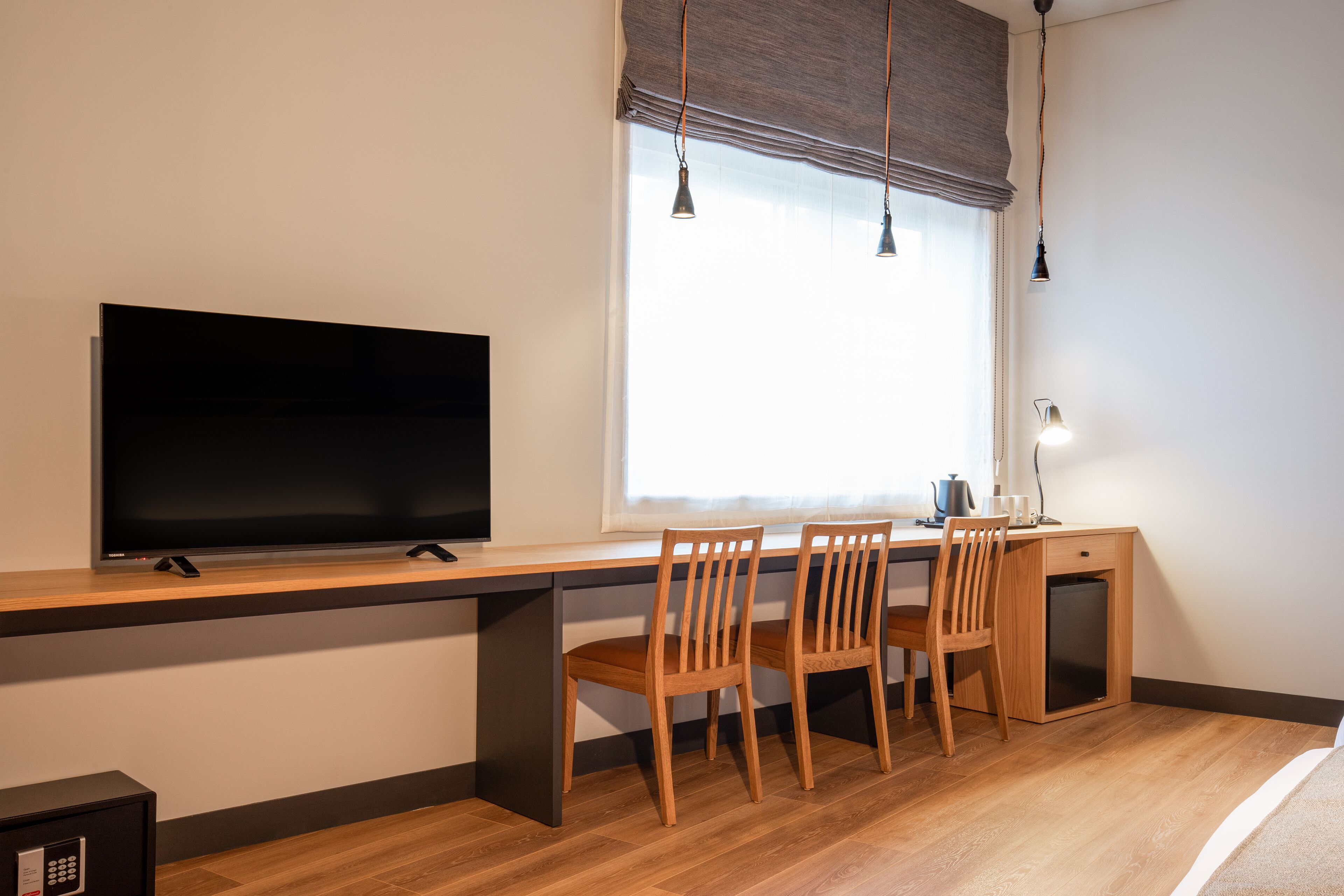 A modern bedroom with a wooden desk, two chairs, a television, and a bedside table.