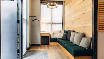 A modern interior with a wooden floor, a green sofa with cushions, a small wooden side table, and a hanging light fixture.