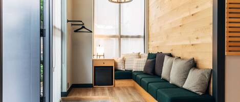 A modern interior with a wooden floor, a green sofa with cushions, a small wooden side table, and a hanging light fixture.