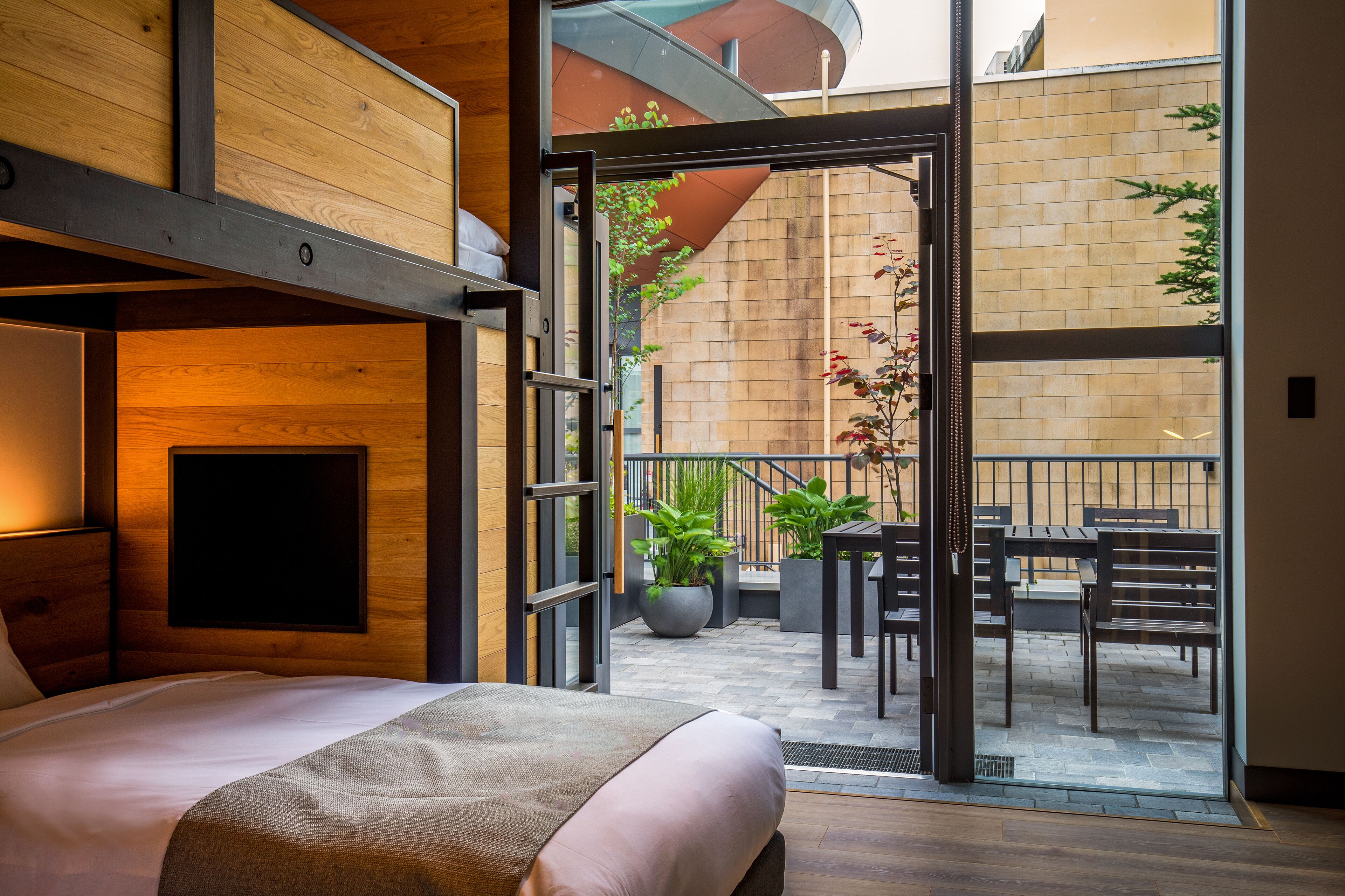 Une chambre d’hôtel moderne dotée d’un lit, d’une grande fenêtre et d’un balcon aménagé avec du mobilier d’extérieur.