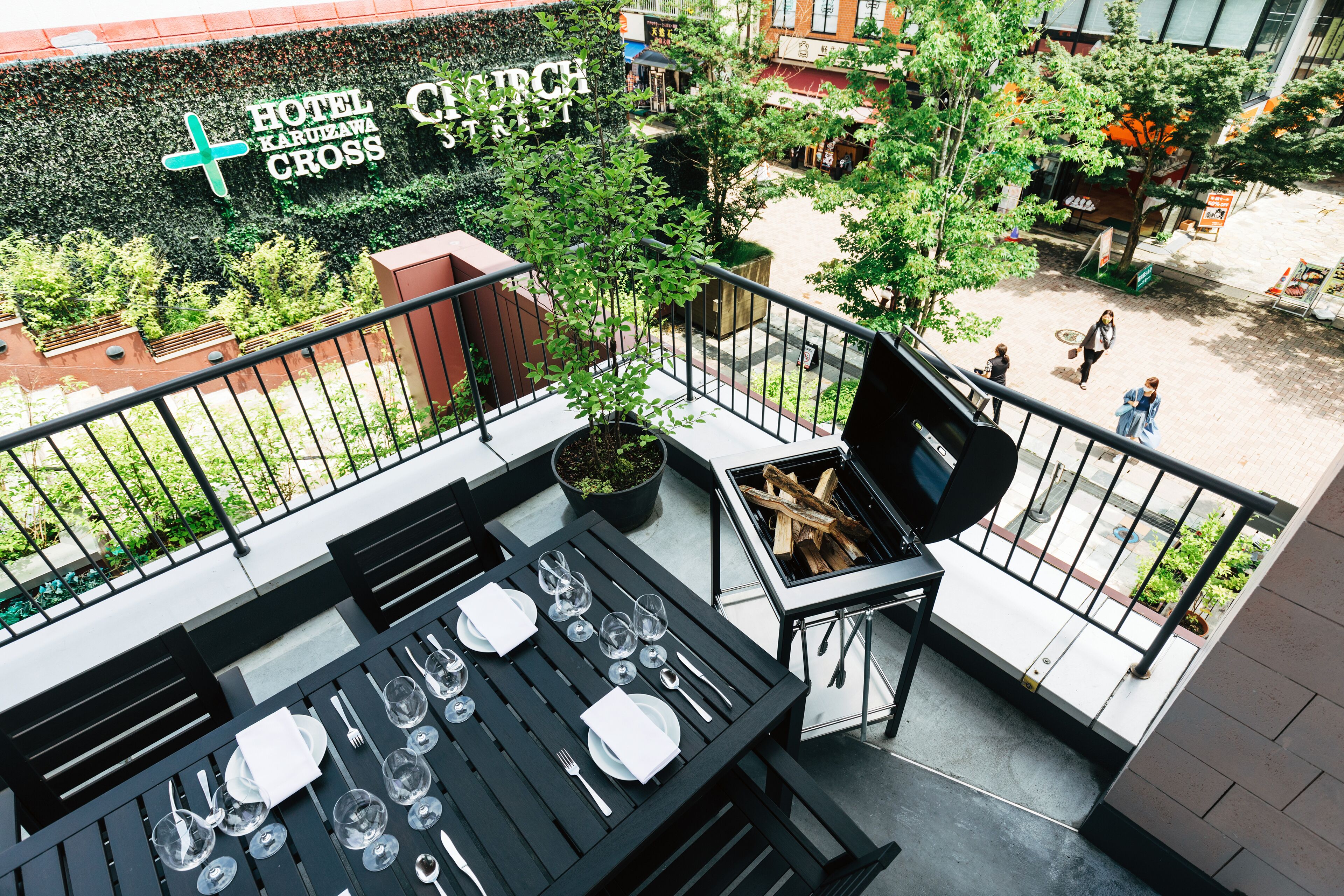 A rooftop terrace with a dining table set for six, a grill, and a view of the street below.