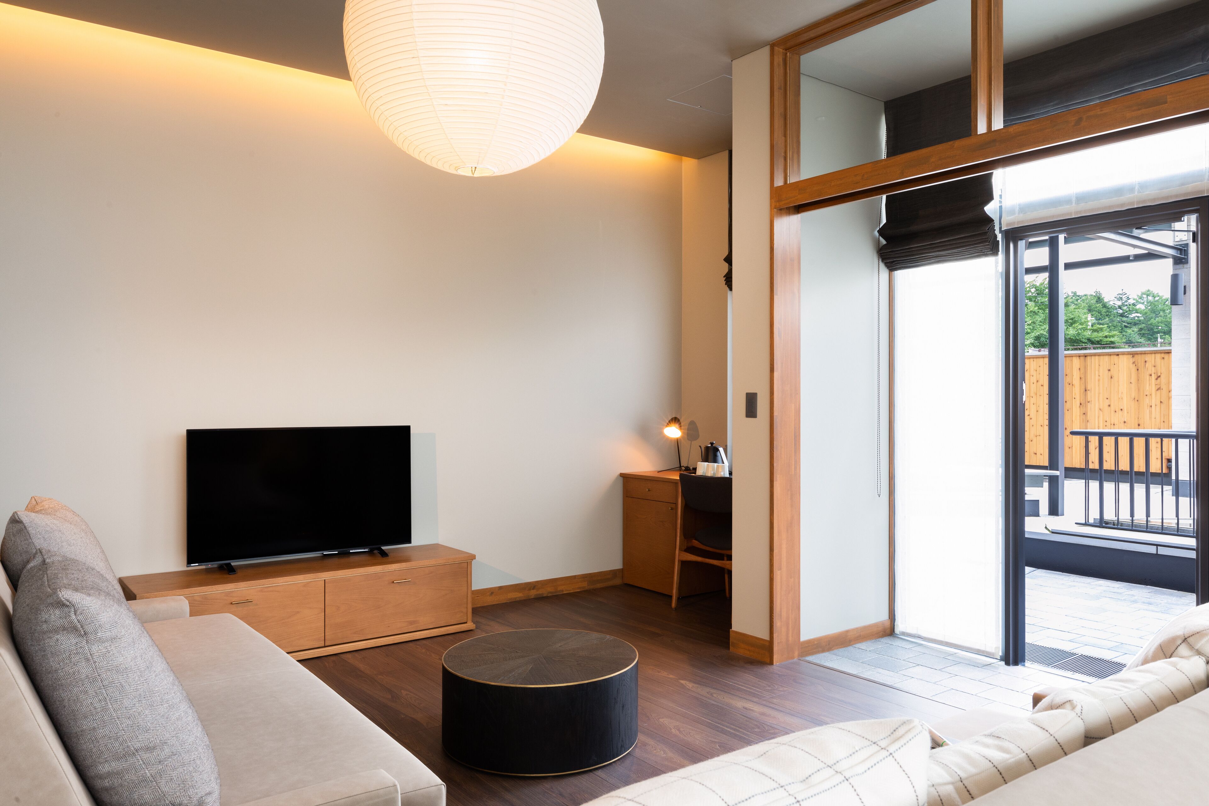 Un salon moderne comprenant un téléviseur à écran plat, un canapé, un pouf rond et un bureau avec une chaise.