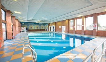 An indoor swimming pool with checkered floor tiles, clear blue water, and a view of the outside through large windows.