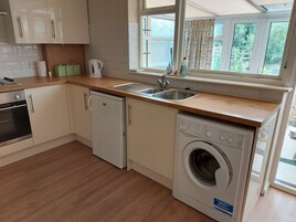 Uma cozinha compacta com máquina de lavar louça, pia e janela com cortinas.