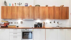 A modern kitchen with wooden cabinets, a built-in oven, and various kitchen appliances. - Beautiful 1 Bedroom Apartment in Shepherd's Bush (London)