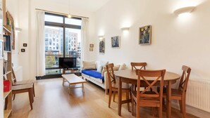A modern living room with a sofa, a dining table with chairs, a TV, and a bookshelf. - Beautiful 1 Bedroom Apartment in Shepherd's Bush (London)