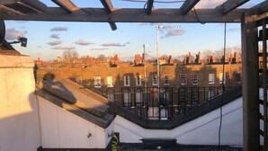 A rooftop terrace with a view of neighboring buildings, a metal railing, and a hose on the ground. - Stylish and Spacious Apartment With Terrace (London)