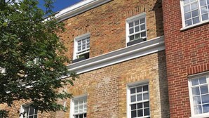 A two-story brick building with a blue facade, white window frames, and a black door. - Stylish and Spacious Apartment With Terrace (London)