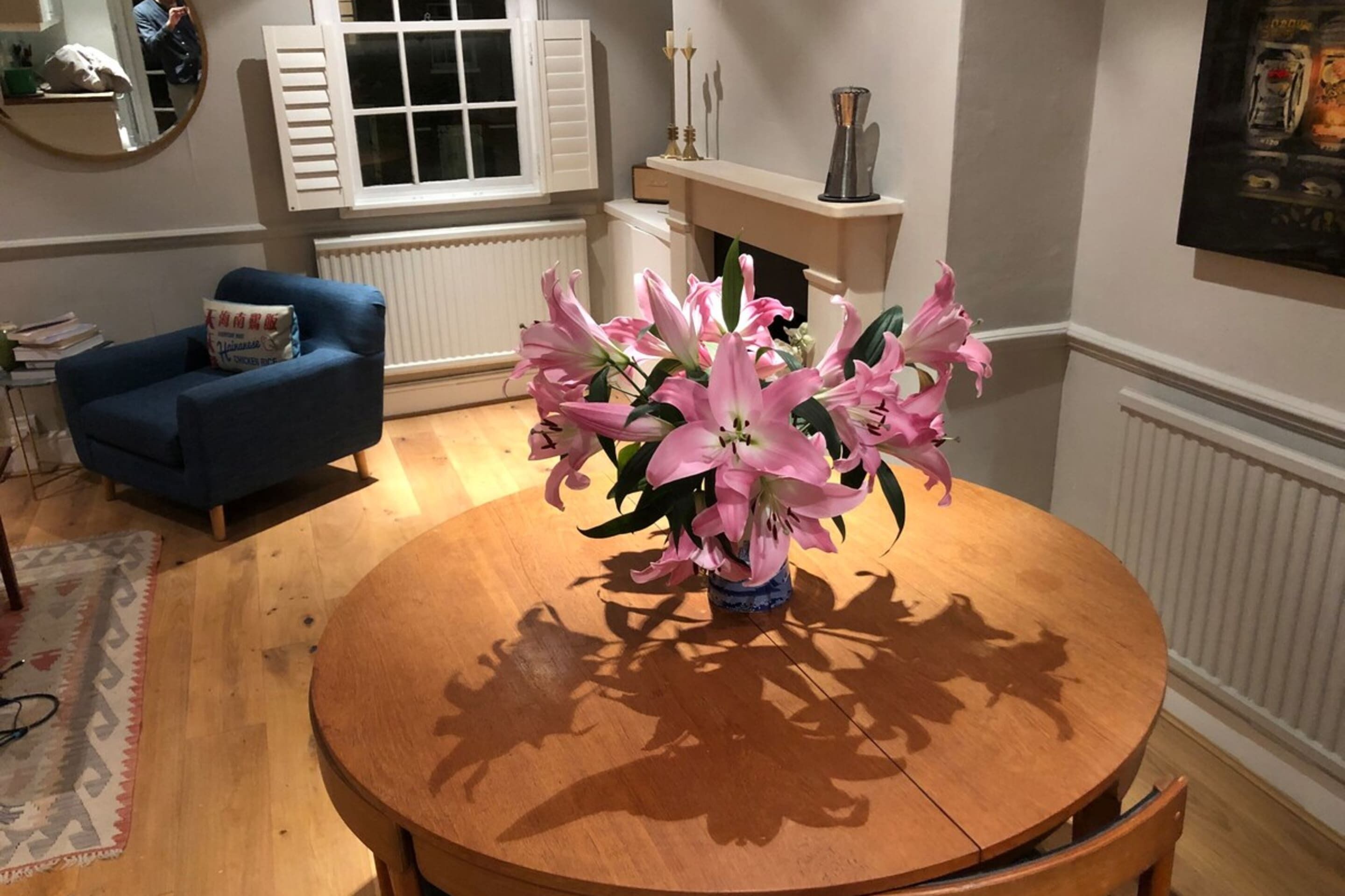 A round wooden dining table with a vase of pink lilies in the center.